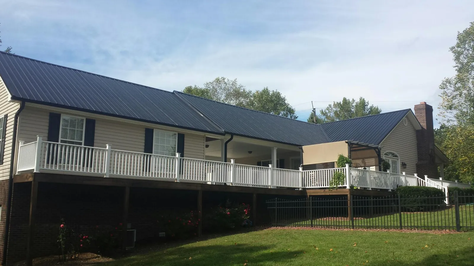 Black metal roof above a long white railed deck on a hillside home in Seymour